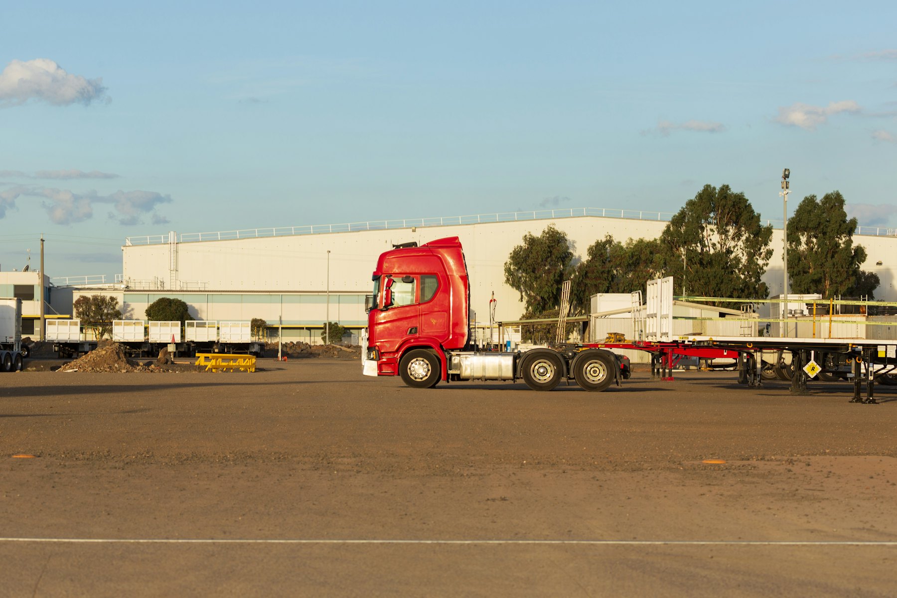 A tractor staged on the yard beside empty flatbed trailers.